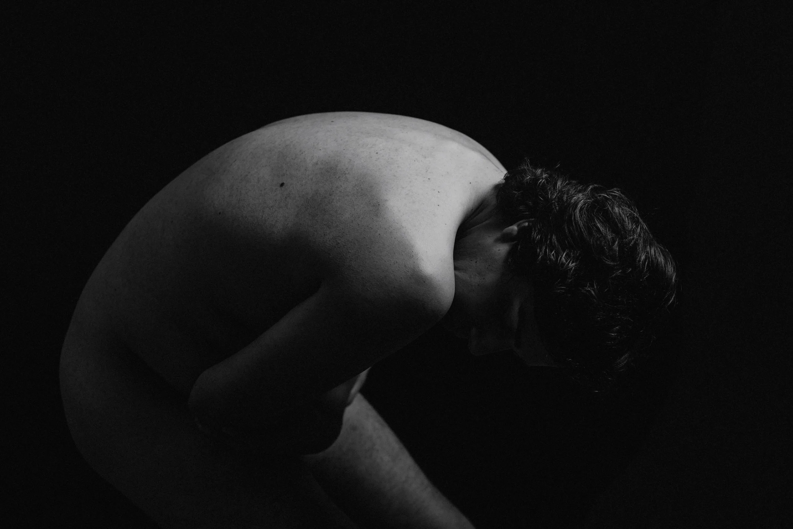 Cuerpo masculino inclinado sobre sí mismo en claroscuro — Manifiestos del Alma